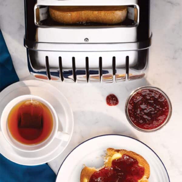 Dualit DA0144 6 Slice Vario Toaster in polished stainless steel with toast, tea, and jam on a table.